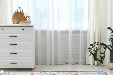 Stylish furniture and houseplant near window with curtains in living room. Interior design