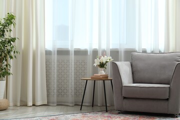 Stylish furniture and houseplant near window with curtains in living room. Interior design