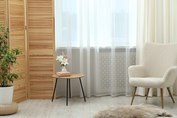 Stylish furniture and houseplant near window with curtains in living room. Interior design