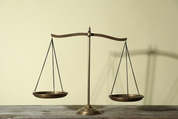 Golden scales of justice on wooden table against beige background