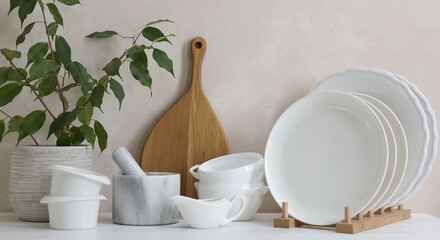 Different clean white dishware, wooden cutting board and houseplant on counter in kitchen