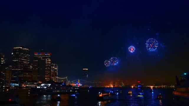 The East River with multiple boats standing on the anchor. Night view of New York celebrating the holiday with fireworks.