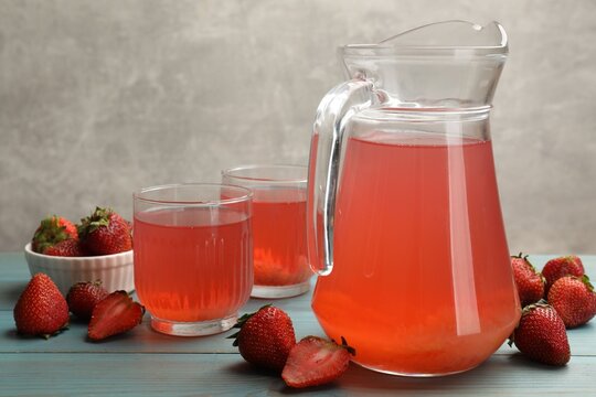 Tasty compot in glasses, jug and fresh strawberries on light blue wooden table, closeup