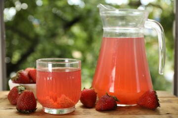 Tasty compot in glass, jug and fresh strawberries on wooden table outdoors, closeup