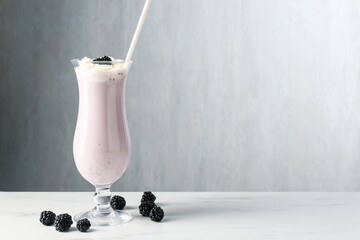 Tasty blackberry milkshake with whipped cream in glass and berries on white marble table, space for...
