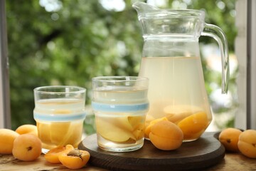 Tasty compot with apples in glasses, jug and fresh apricots on wooden table outdoors, closeup
