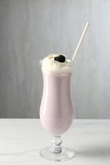 Tasty blackberry milkshake with whipped cream in glass on white marble table