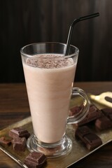Tasty milkshake in glass and pieces of chocolate on wooden table, closeup