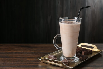 Tasty milkshake in glass and pieces of chocolate on wooden table, space for text
