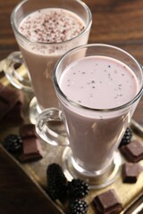 Different tasty milkshakes in glasses and ingredients on wooden table, closeup