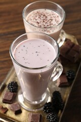 Different tasty milkshakes in glasses and ingredients on wooden table, closeup