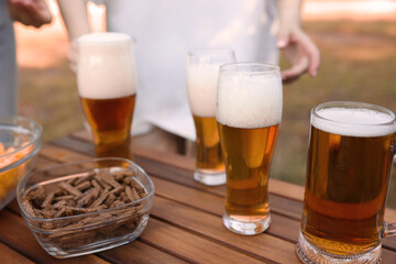 Glasses of beer and snacks on wooden table outdoors, closeup