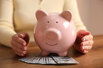 Woman with piggybank and money at wooden table, closeup