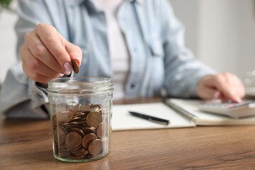Fototapeta premium Woman counting and putting coins into jar at wooden table, selective focus