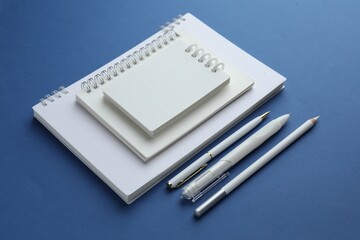 White notebooks, pencil and pens on blue background