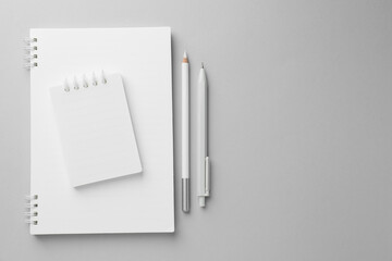 White notebooks, pen and pencil on light grey background, top view. Space for text