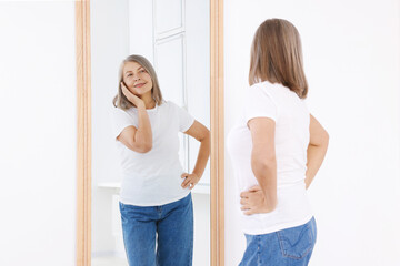 Beautiful senior woman looking at herself in mirror indoors. Mental health