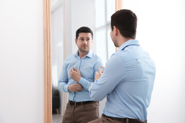 Man looking at serious reflection of himself in mirror indoors. Mental health