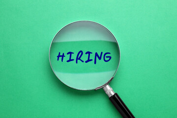 Word Hiring on green background, view through magnifying glass
