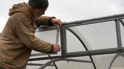 Step-by-step construction of an arched greenhouse. An adult man cuts polycarbonate for the upper...