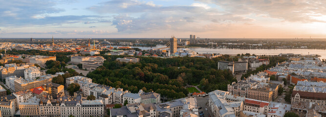 Obraz premium Riga, Latvia at sunset featuring Jugendstil architecture, a central park, the Daugava River, Riga TV Tower, church spires, and modern buildings.
