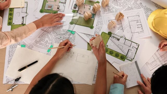 Architect and engineer consider or discuss about building construction using blueprint on table with architectural document, measurement tool and wooden block scatter around at office. Delineation.