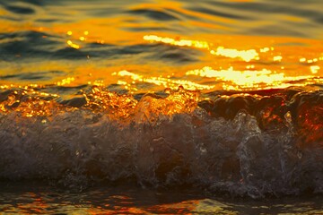 Golden sea waves with foam sparkle and shine in beautiful sunset on the beach summertime background