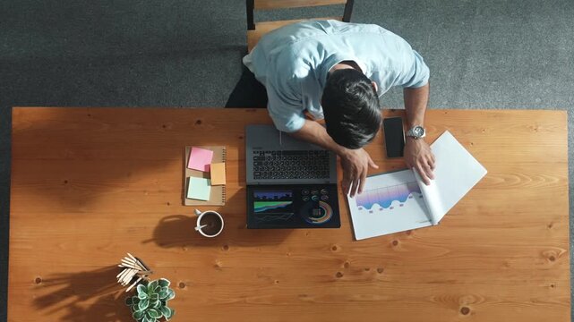 Top aerial view of manager working on laptop while looking at data analysis. Leader compare financial statistic graph while making decision at meeting table with document scatter around. Convocation.