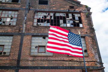 American flag waves in front of an abandoned factory with broken windows, symbolizing the decline of U.S. manufacturing and its shift overseas amid U.S.-China trade tensions