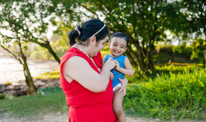 Fototapeta premium Mother tenderly hugs her young son while sharing a moment together on the riverbank during summer vacation.