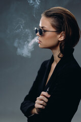 Profile of a stylish woman smoking with sunglasses and dark clothing in a moody setting with smoke.