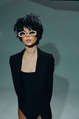 Stylish woman with short hair wearing white sunglasses and black blazer posing confidently in...
