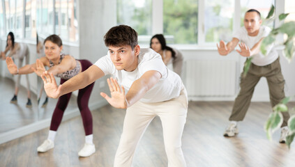 Obraz premium Young guy enjoys dancing, learning to twerk during group class at studio school for young people. Devotion of modern trend pastime, active lifestyle and hobbies