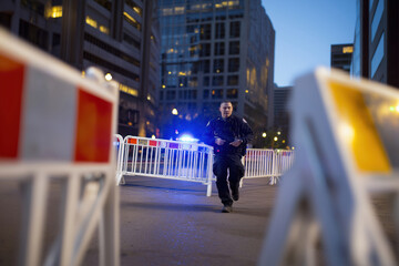 Police officer responds to an emergency in a city street at dusk with barricades