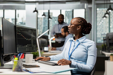 Trader in brokerage firm office analyzing market metrics and executing trades using trading app...