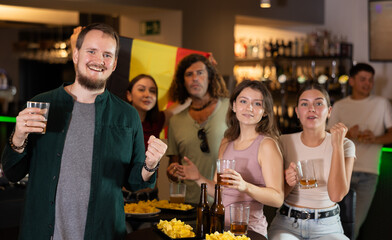 Group of friends fans watching match cheering with Belgian flag in bar