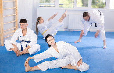 Sports team in kimono doing muscle stretching before karate or judo training