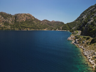 Aerial view of a winding coastal road skirting a deep blue bay near Mugla Turkiye Cliffs and pine...