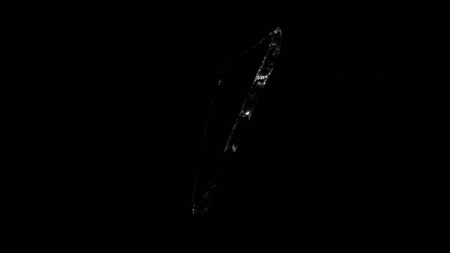 Long narrow shard of broken glass, resembling a dagger splinter, slowly rotating and flashing from reflected light.