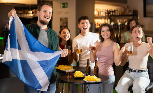 Group of friends fans watching match cheering with Scottish flag in bar