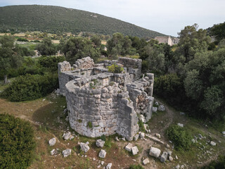 Aerial view of round tower ruin at patara among olive trees, rugged limestone blocks, council house...