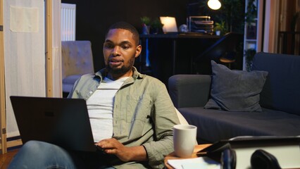 Young black person waving on remote video call on laptop sitting at home, joining an online...