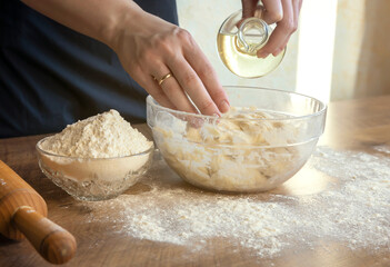 Close-up of female hands adding oil to the dough, on the background of flour and a rolling pin, the concept of home baking.