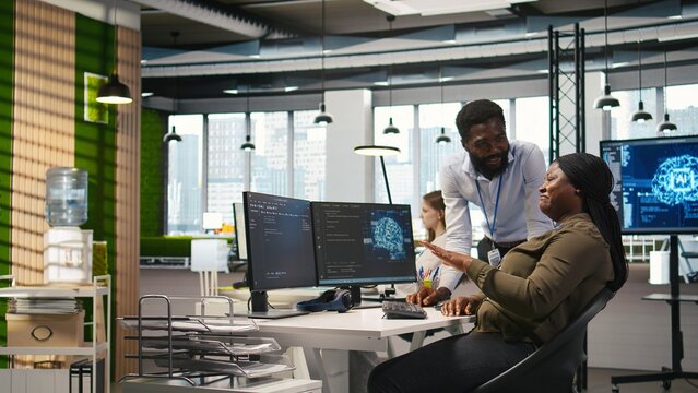 Happy engineers enjoying funny conversation at desk while using AI on computer to optimize performance. Cheerful colleagues in office chatting, training deep learning models using PC, camera A - Powered by Adobe