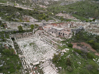 Overcast skies frame stone seating and stage remnants of Sagalassos ancient theater carved into hillside surrounded by lush vegetation in Turkish mountains preserving Roman era archaeological wonder