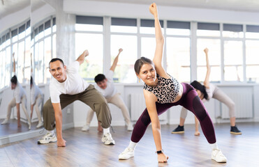 Cheerful emotional sporty young female dancer rehearsing popping techniques during group workout in...