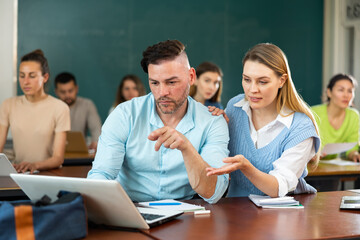 Man and woman solving a problem together on a laptop while studying in a university classroom
