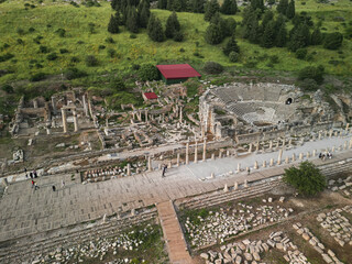 Aerial view reveals the small theatre and colonnaded street at Ephesus, rows of seats curve by the stage, columns line the avenue below, ancient Turkey's cityscape spreads across the hillside