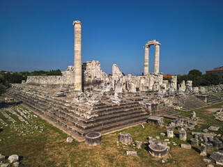 Aerial view of the temple of apollo at didyma, colossal podium and a lone standing column command the ruins, limestone terraces guide the eye, visitors explore archaeology in Turkey under a clear sky