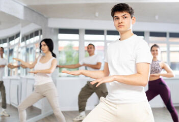 Enthusiastic sporty smiling Hispanic guy energizing group of young people during dance fitness...